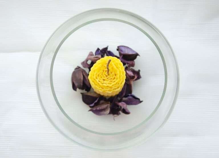 Yellow candle surrounded by purple dried petals in a clear glass bowl, viewed from above.